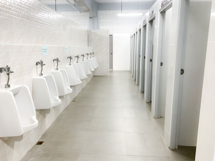 Public restroom with urinals and stalls, highlighting hidden needle marks in toilet paper as a new fear unlocked.