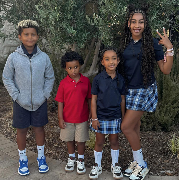 Children posing outdoors in casual and school attire, smiling in front of greenery.