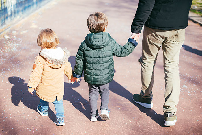 Man walking with two children, holding hands, outdoors on a sunny day, symbolizing desire for kids in relationships. Man walking with two children, holding hands, outdoors on a sunny day, symbolizing desire for kids in relationships.