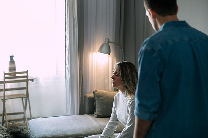 Man standing near a woman on a sofa, engaging in conversation about wanting kids, with a lamp softly illuminating the room. Man standing near a woman on a sofa, engaging in conversation about wanting kids, with a lamp softly illuminating the room.
