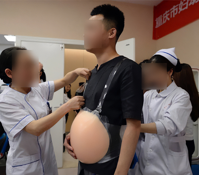 Man participating in childbirth simulation, assisted by nurses, with a pregnancy suit in a hospital setting. Man participating in childbirth simulation, assisted by nurses, with a pregnancy suit in a hospital setting.