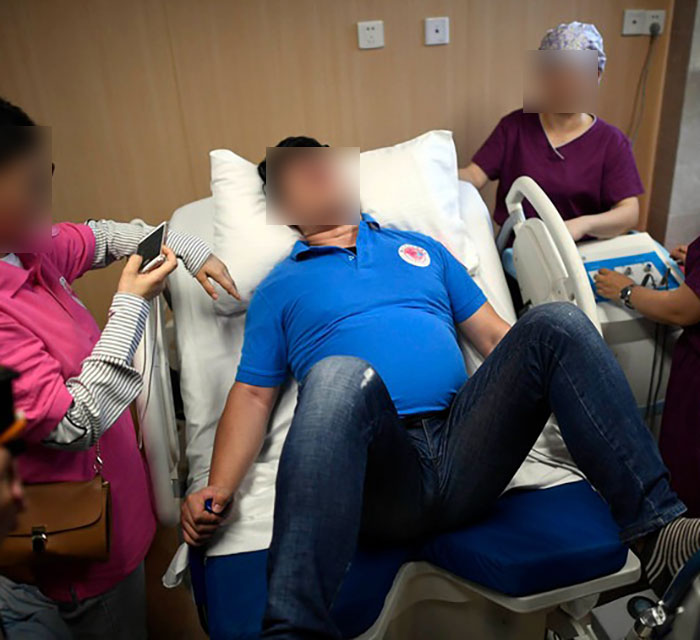 Man undergoes childbirth simulation in hospital, surrounded by medical staff. Man undergoes childbirth simulation in hospital, surrounded by medical staff.