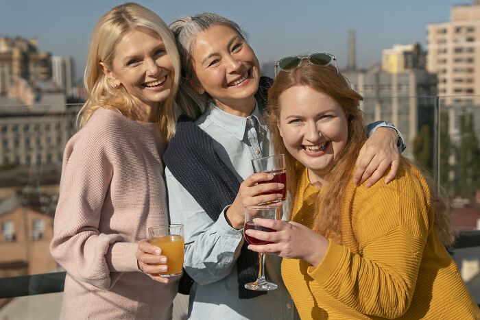 Three smiling women enjoying drinks on a rooftop, representing a childfree friend group gathering.