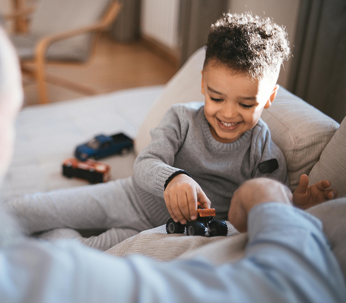 Child happily playing with toy cars on a sofa, interacting with a friend, creating a joyful holiday atmosphere. Child happily playing with toy cars on a sofa, interacting with a friend, creating a joyful holiday atmosphere.