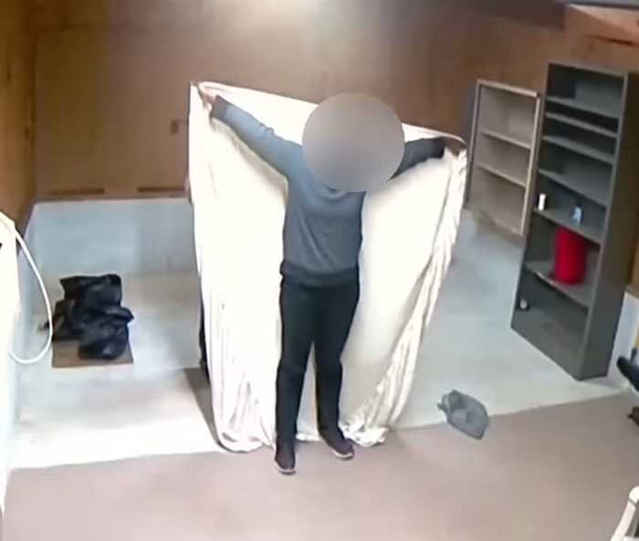 Person holding a large sheet in a sparsely furnished room, with shelves in the background. Person holding a large sheet in a sparsely furnished room, with shelves in the background.