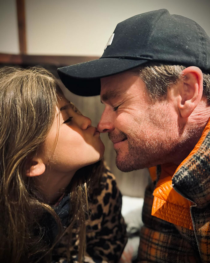 Man and child sharing a tender moment, causing online outrage, wearing warm clothes indoors. Man and child sharing a tender moment, causing online outrage, wearing warm clothes indoors.