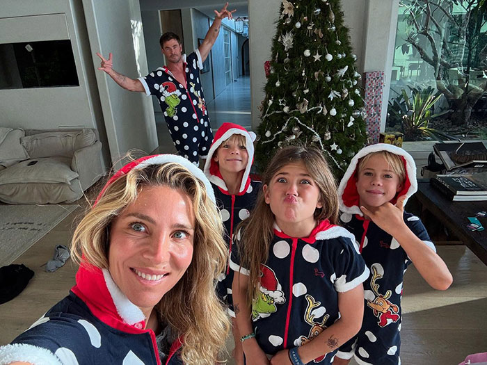 Chris Hemsworth and family in holiday pajamas pose near a Christmas tree at home.