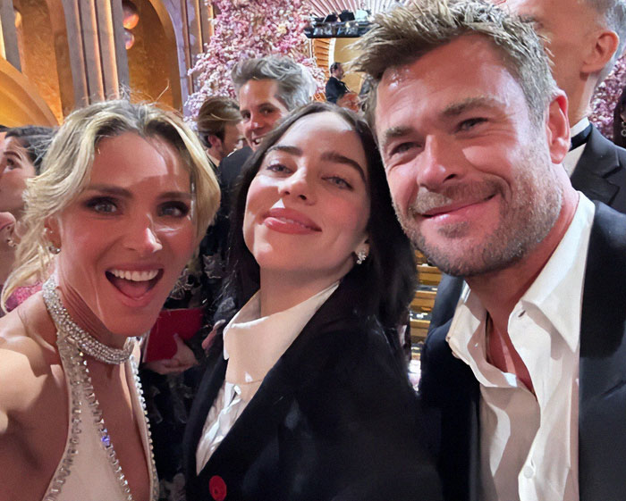 Celebrity selfie at Oscars with smiling attendees, capturing a memorable moment in a crowded, glamorous setting.