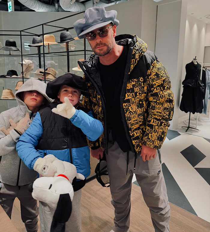 Man in a stylish jacket with two kids in a store, surrounded by hats, sparking photo controversy. Man in a stylish jacket with two kids in a store, surrounded by hats, sparking photo controversy.