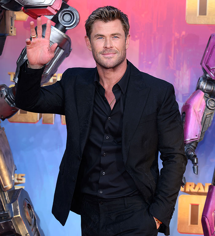 Chris Hemsworth smiling in a suit at an event, colorful background.