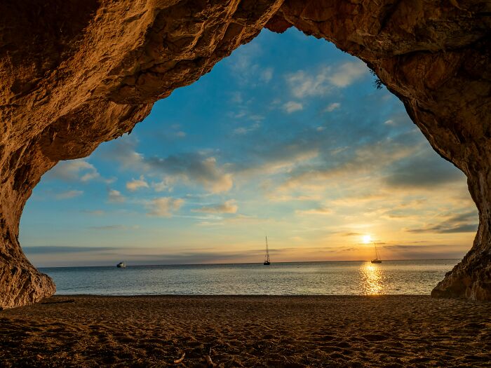 Sunset view through a beach cave opening with boats on the horizon, highlighting stunning beaches.