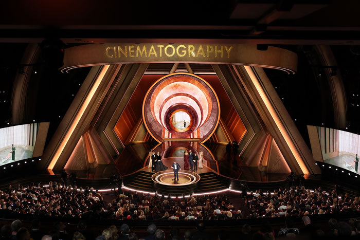 Oscars 2025 ceremony stage with winners receiving an award for cinematography, audience watching.
