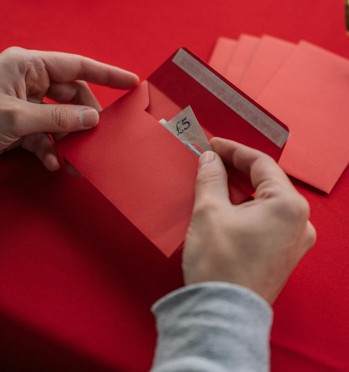Hands placing a £5 note into a red envelope on a table, symbolizing winning an eating competition for easy money.