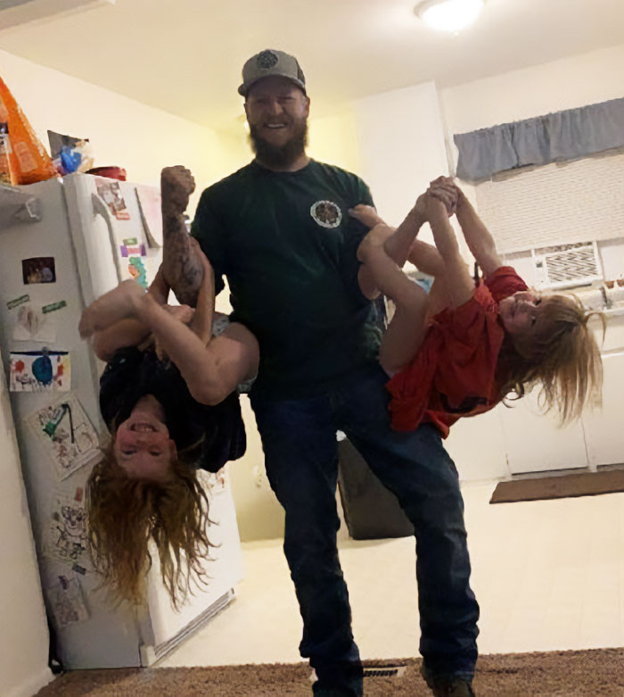 A joyful moment in a kitchen, featuring a man playfully holding two children. A joyful moment in a kitchen, featuring a man playfully holding two children.