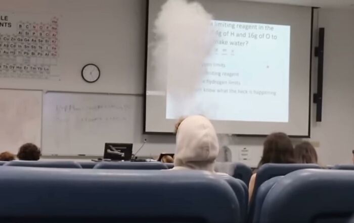 Classroom with a chemistry slide, smoke rising, and people watching, related to entitled behavior.