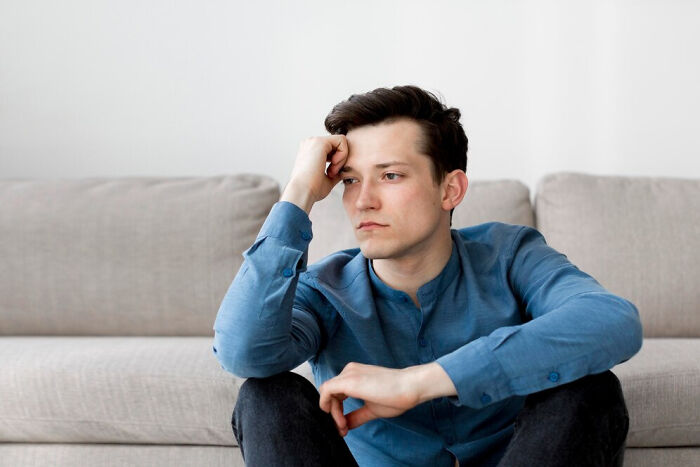 A thoughtful man in a blue shirt sits on a couch, reflecting on former best friends.