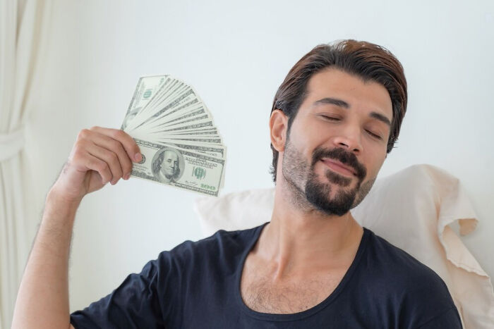 Man smiling and fanning himself with dollar bills, illustrating reasons for not speaking to former best friends.