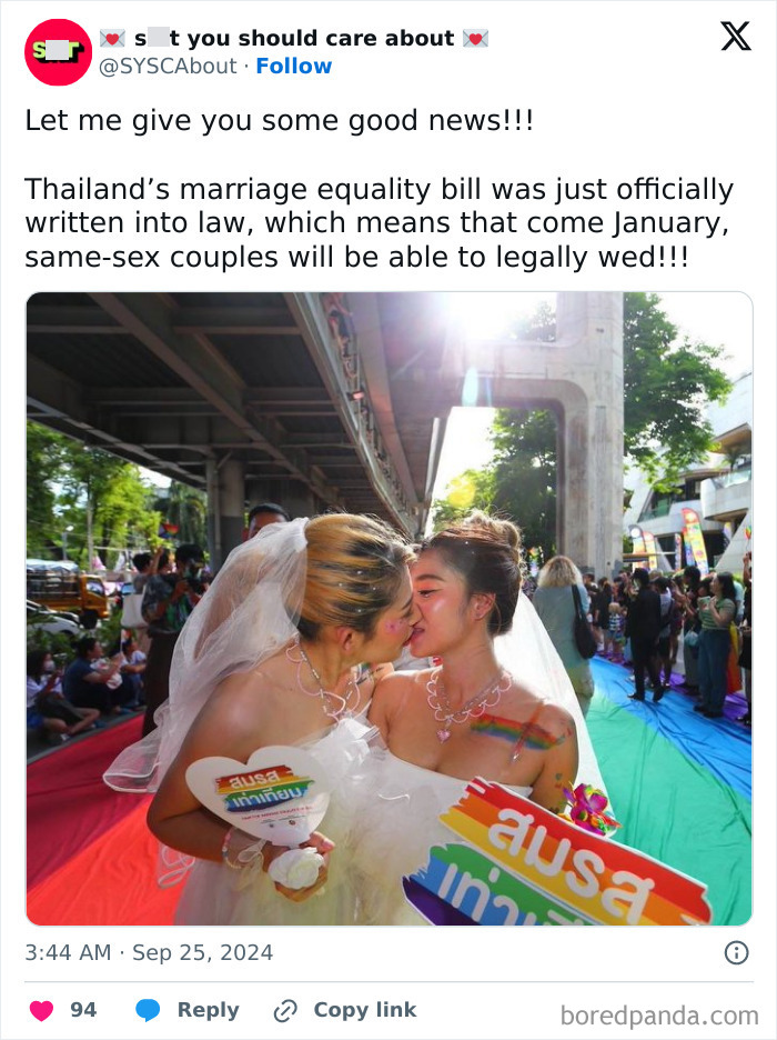 Two brides kissing at a marriage equality celebration in Thailand, holding rainbow-colored signs.