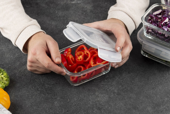 Person placing sliced peppers in a glass container, highlighting impactful kitchen storage solutions.