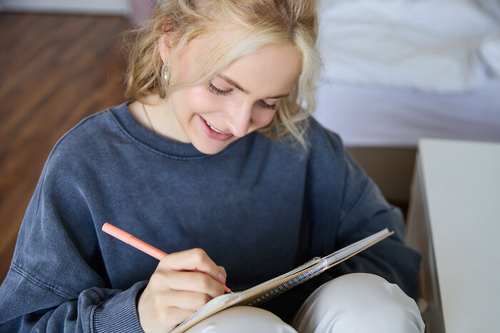 Person smiling while writing in a notebook, highlighting underrated activities that get more hate than they deserve.