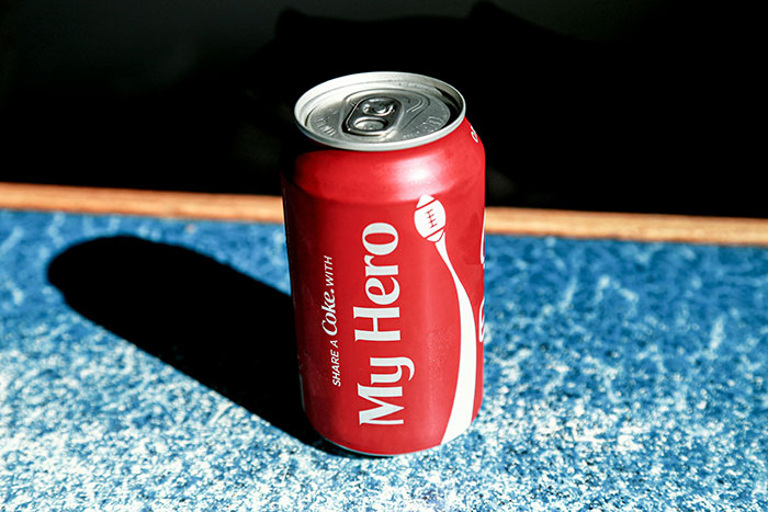 Red soda can labeled "My Hero," symbolizing a tribute on a speckled blue surface. Red soda can labeled "My Hero," symbolizing a tribute on a speckled blue surface.