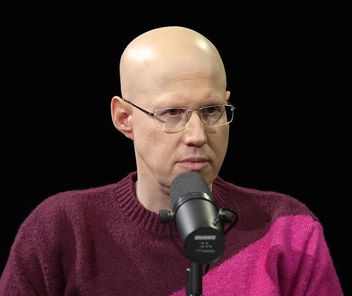 Matt Lucas wearing glasses and a maroon sweater, speaking into a microphone. Matt Lucas wearing glasses and a maroon sweater, speaking into a microphone.