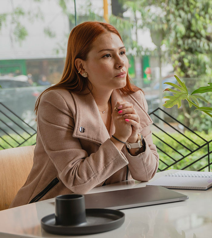 Woman in a beige coat thoughtfully sitting at a table with a laptop and notebook, embodying psychological tricks awareness.