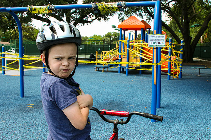 Child with a bike helmet showing a defiant expression in front of a closed playground, highlighting psychological tricks.
