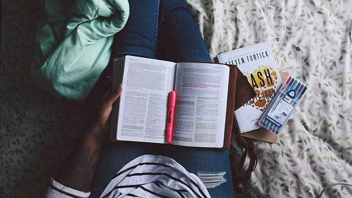 Person reading a book with a pink highlighter, focusing on effective psychological tricks.
