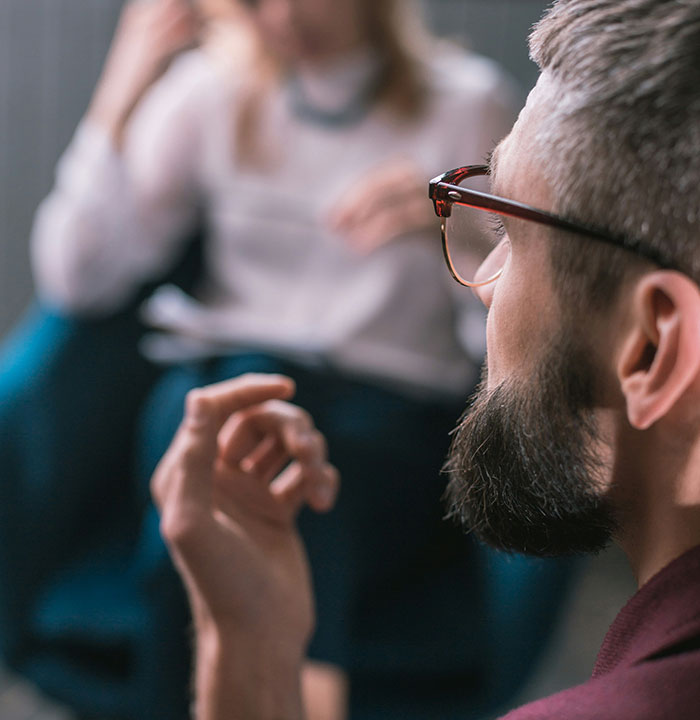 Man using psychological tricks in thoughtful conversation, wearing glasses, with focus on his hand gesture.