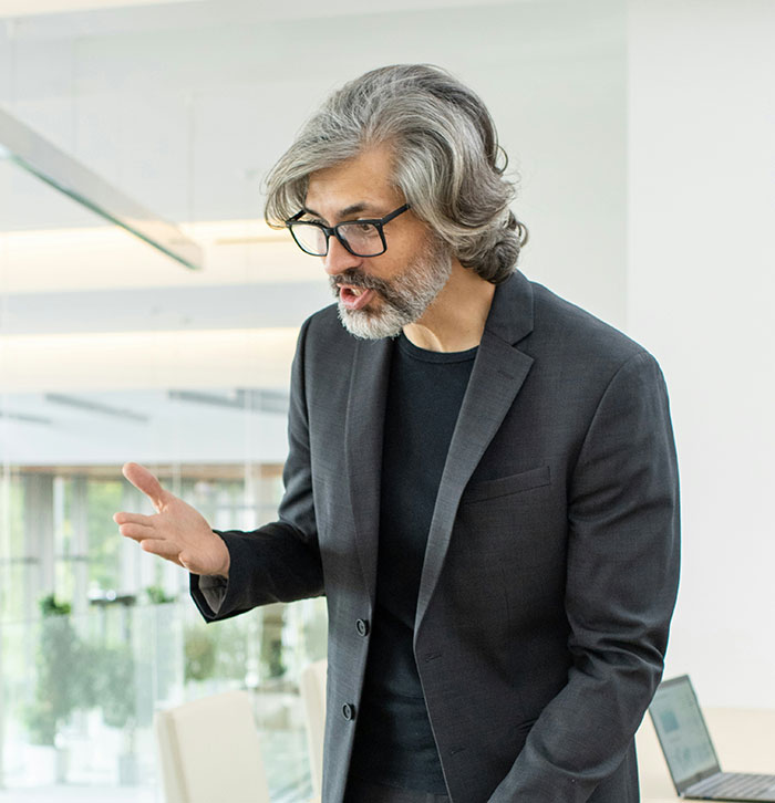 Man in a suit using expressive gestures during a discussion on psychological tricks in a modern office setting.