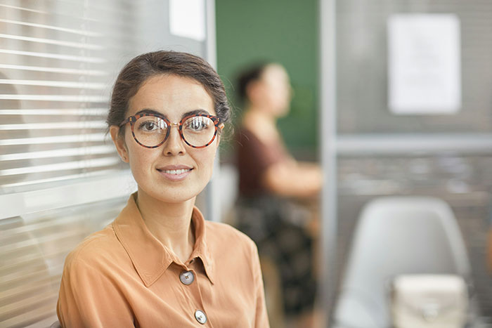 Smiling woman with glasses in an office, illustrating psychological tricks in social settings.