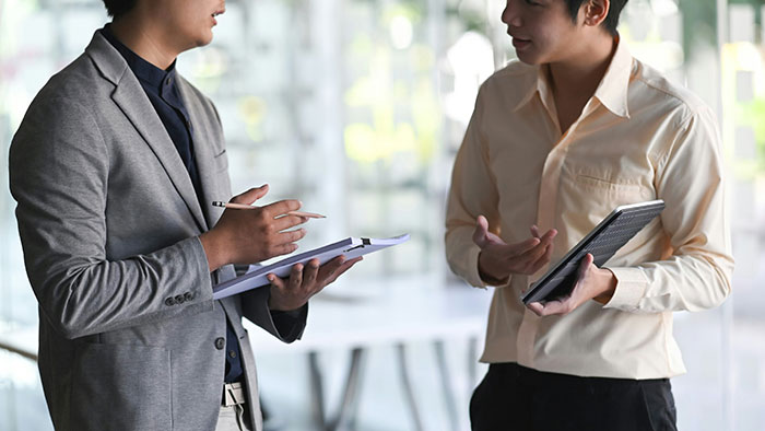 Two people discussing psychological tricks, one using a tablet, the other with a notepad, in a modern office setting.