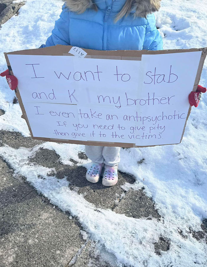 Police officer forces child to stand outside with sign in cold weather.