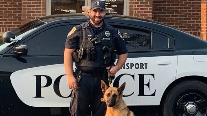 Police officer with a police dog in front of a patrol car.