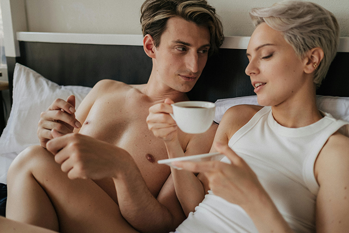 Couple in bed with coffee, discussing coffee-making preferences, highlighting a lazy dispute. Couple in bed with coffee, discussing coffee-making preferences, highlighting a lazy dispute.