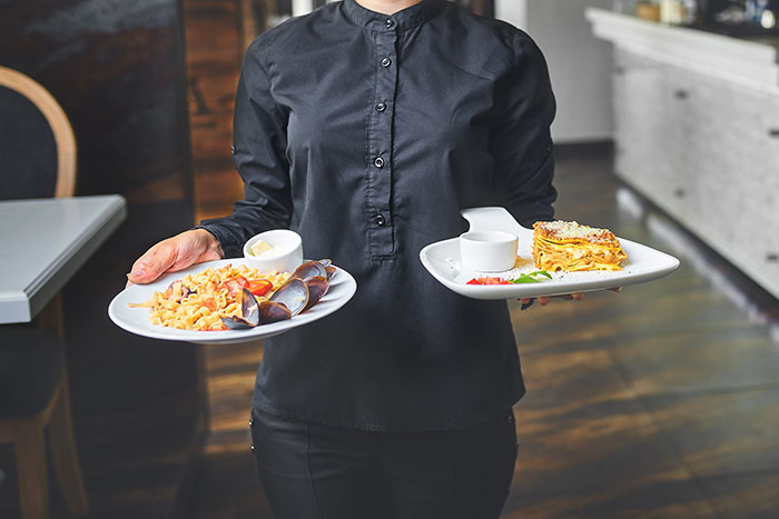 Server holding two plates with meals in a restaurant setting, highlighting rights concerning service animals.