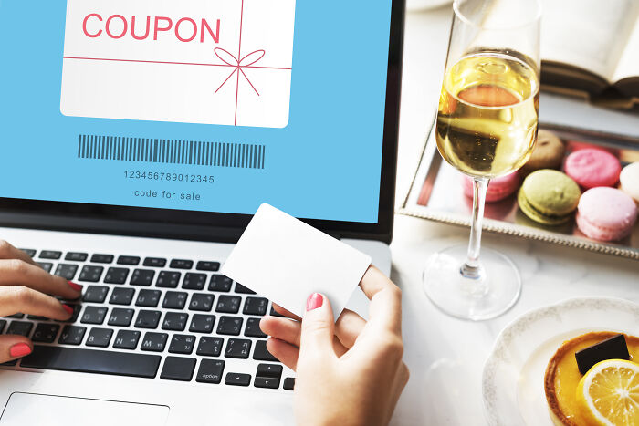 Person using laptop with coupon code on screen; glass of wine and macarons nearby.