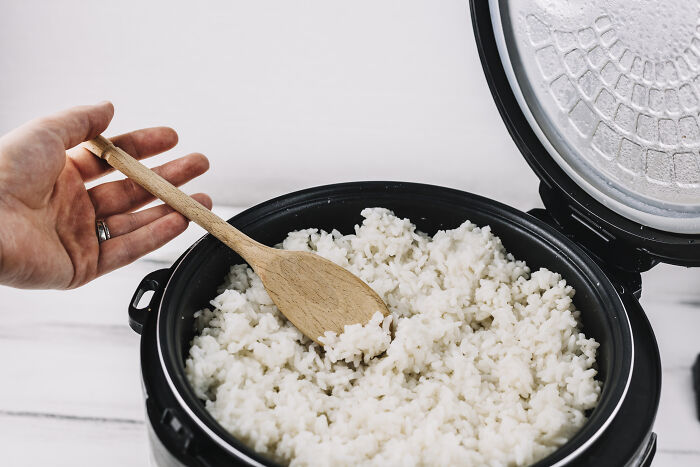 A hand holding a wooden spoon scooping rice from a cooker, highlighting an impactful lifestyle purchase.