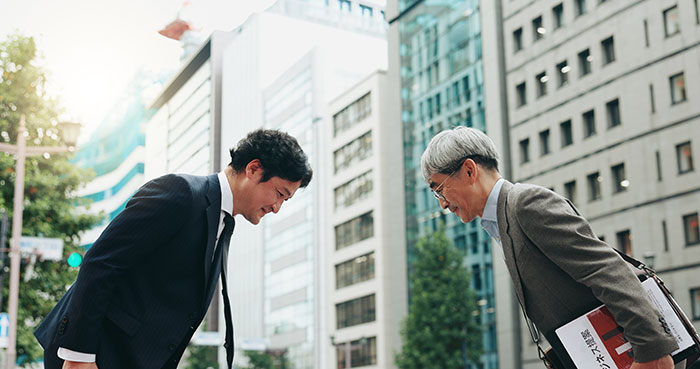Two individuals bowing in a cityscape, illustrating unexpected cultural differences among travelers.