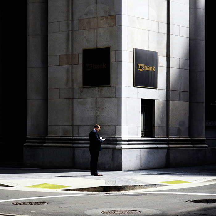 A person in business attire stands by the corner of a US bank building, highlighting cultural differences in urban architecture.