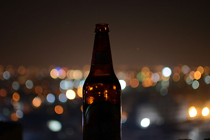 Beer bottle against a city nightscape, highlighting cultural differences in night-time social settings.