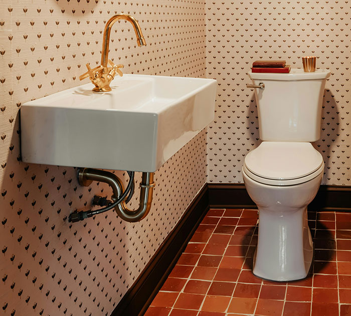 Bathroom showcasing unexpected cultural differences with a gold faucet sink and patterned wallpaper.
