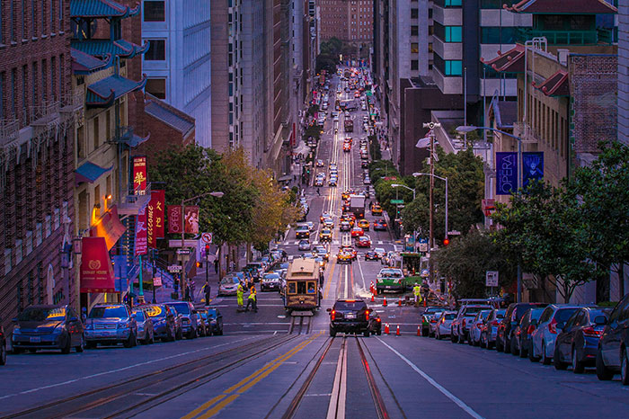 Busy city street with a cable car and cars, showcasing unexpected cultural differences in urban transportation.