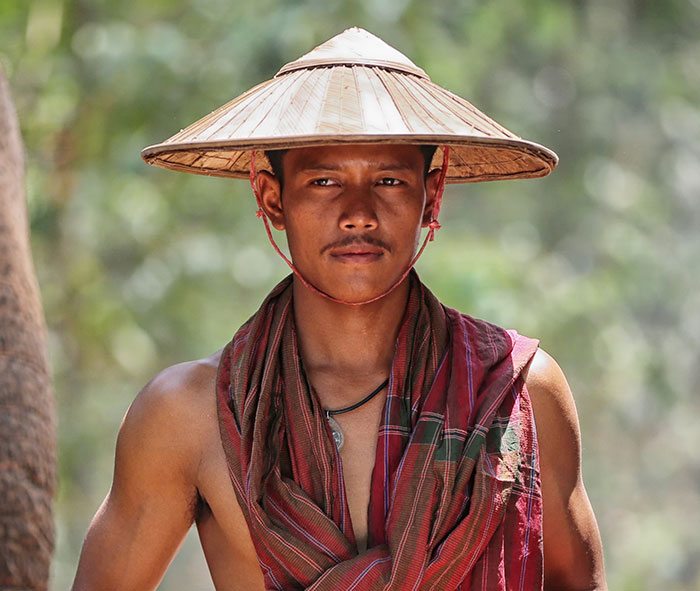 Man wearing traditional Asian attire and conical hat, representing cultural differences in clothing.