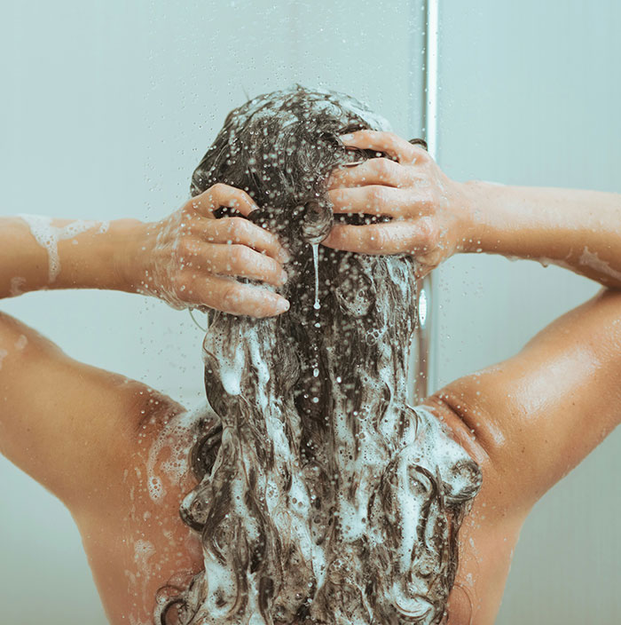 Person washing hair under shower, illustrating unexpected cultural differences in personal hygiene practices.