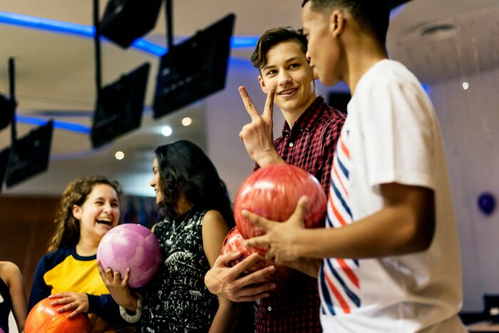 Teens at a bowling alley sharing laugh; a "mess around, find out" moment with bowling balls in hand.