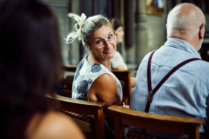 Woman smiling at a wedding, wearing glasses and floral dress, seated next to a man.