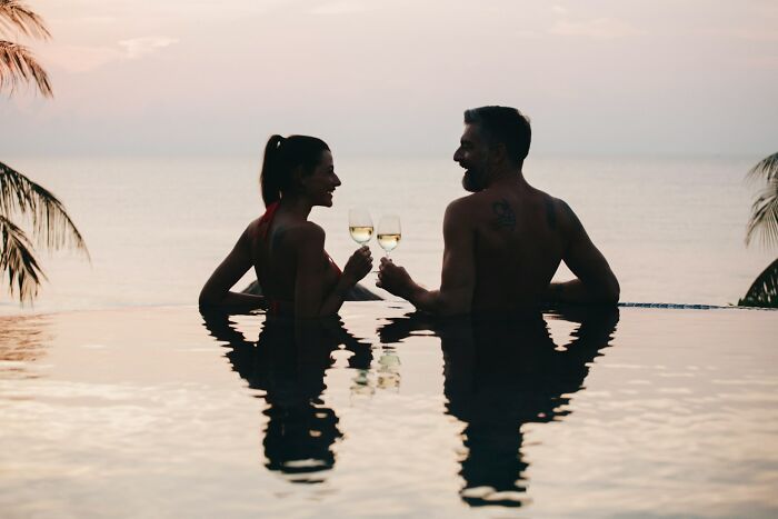 Couple enjoying wine in an infinity pool at sunset, with ocean view.