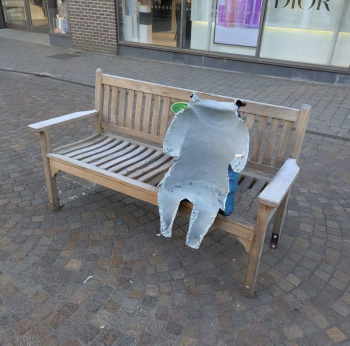 Cut Paddington Bear statue on a bench in town square, military personnel involved.